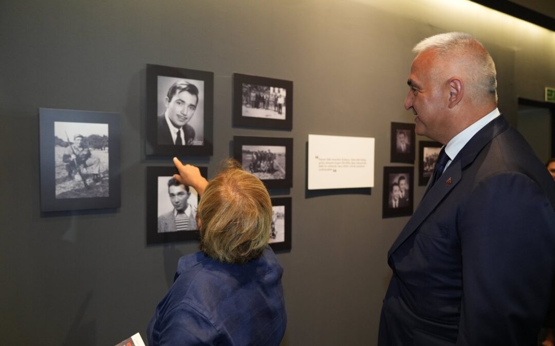 Two people looking at framed photographs on a wall.