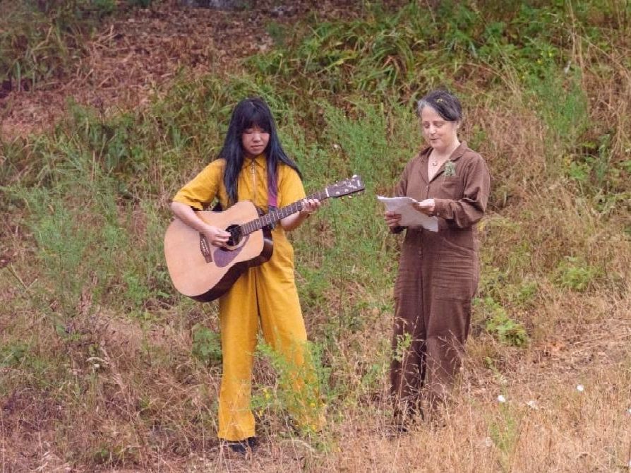 Two people, one plays guitar, outdoor setting