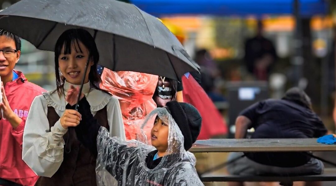 People under umbrella in rainy outdoor event.