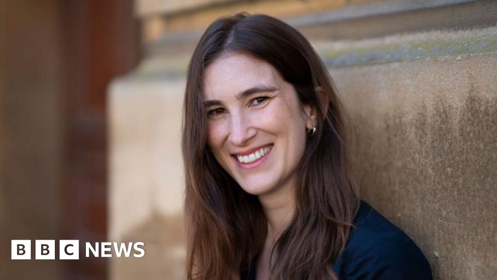 Woman smiling beside a wall, BBC News