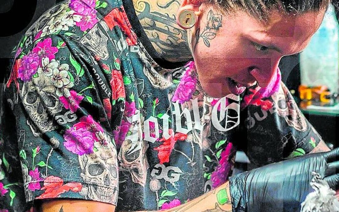 Tattooed artist wearing floral shirt working on a tattoo