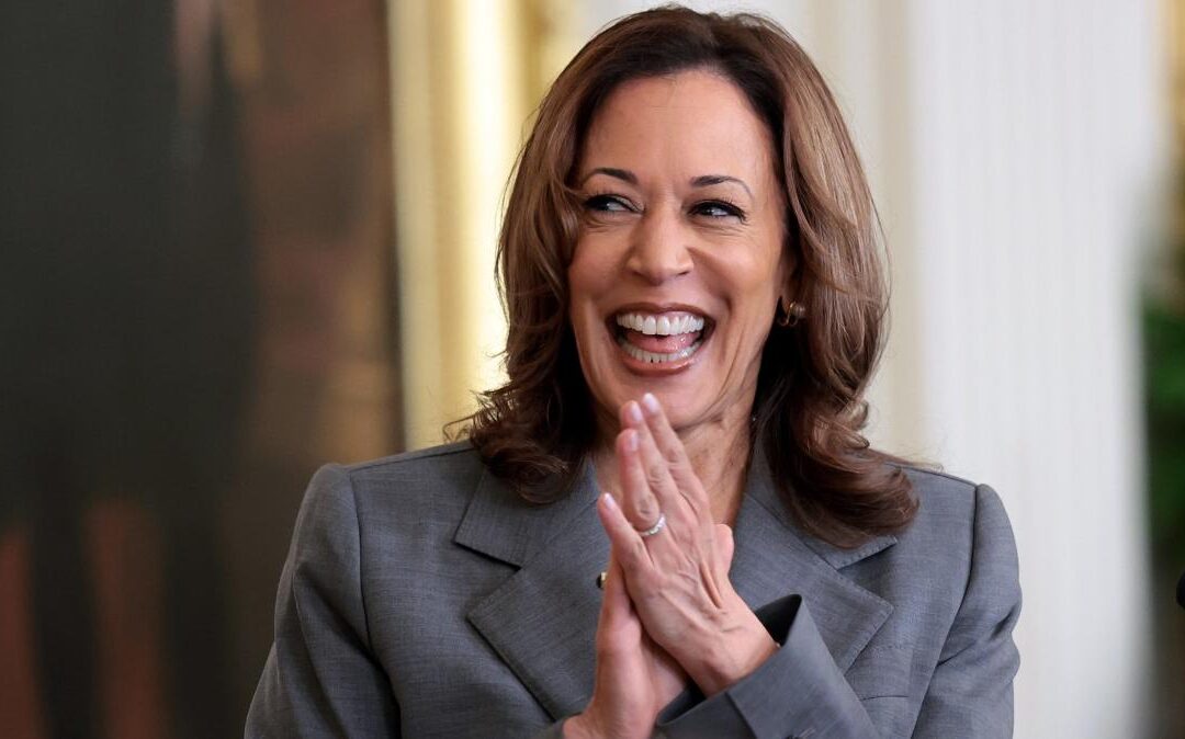 Smiling woman clapping hands in gray blazer.
