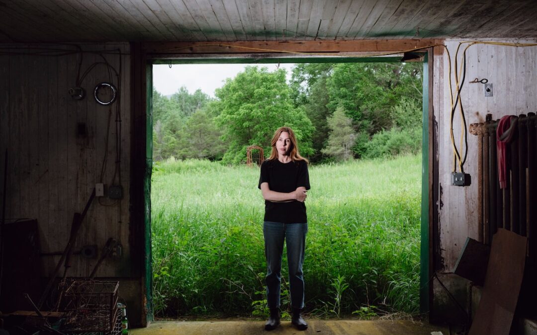 Person standing in doorway with green field backdrop.