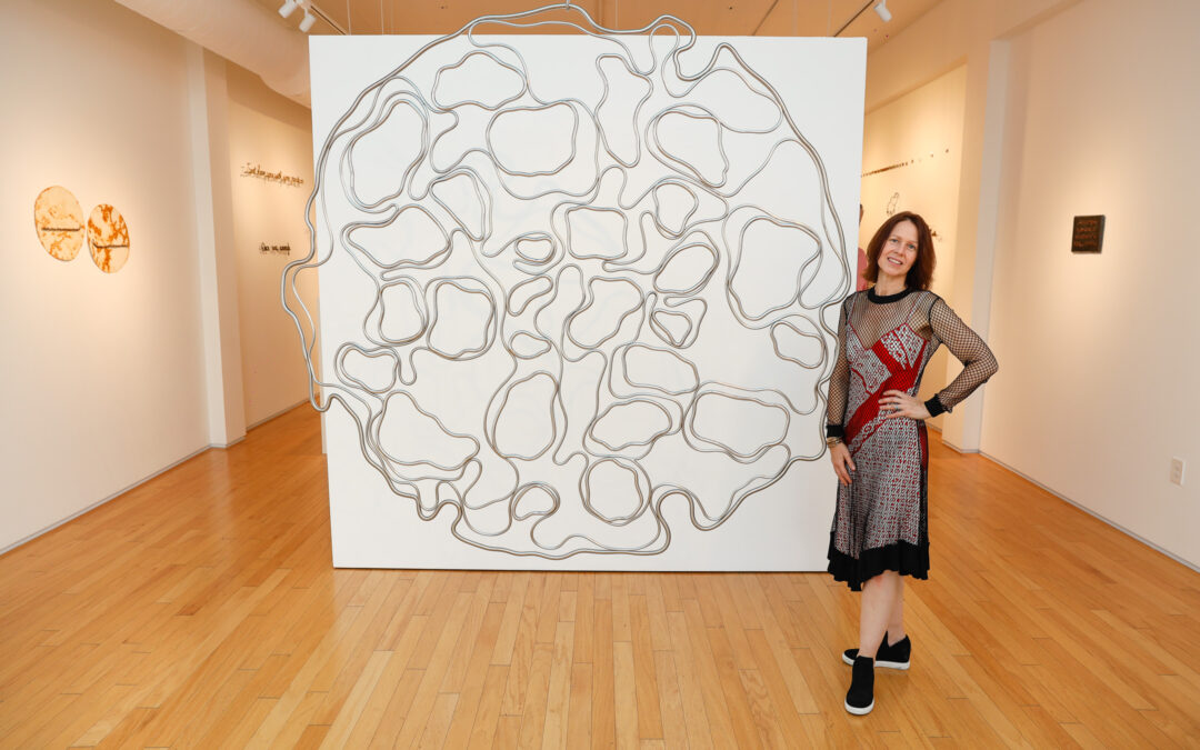 Artist posing with abstract wall art in gallery.