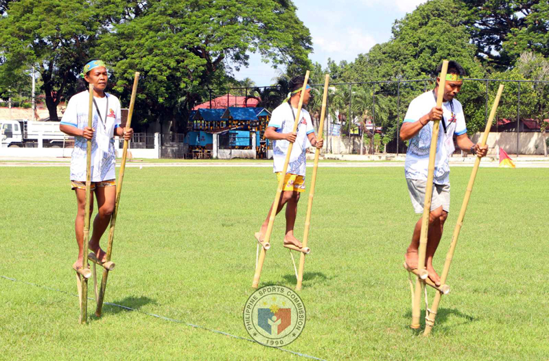 People balancing on bamboo stilts outdoors.