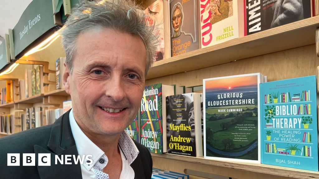 Smiling man in bookstore with shelves of books.