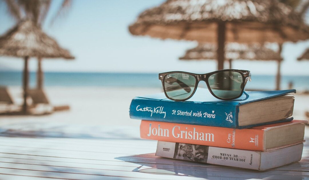 Sunglasses on beach books stack, seashore backdrop