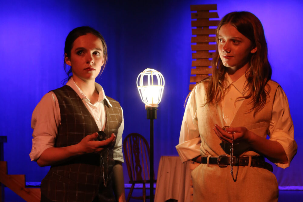 Two actors on stage with a vintage lamp.