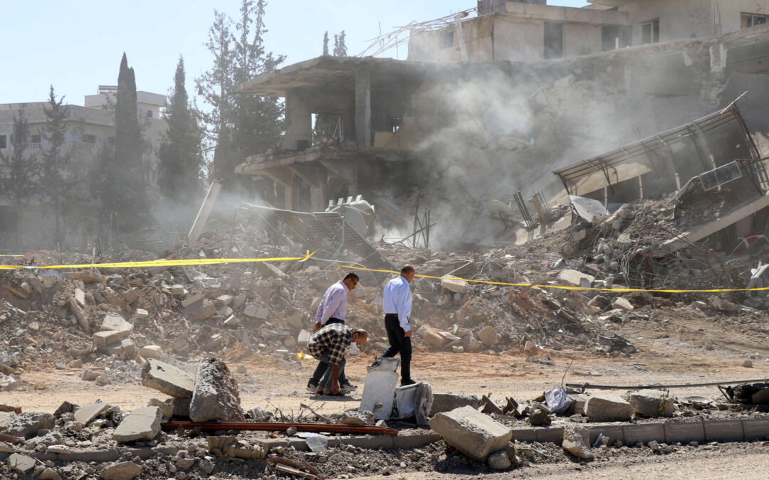 Three people inspect building rubble after destruction.