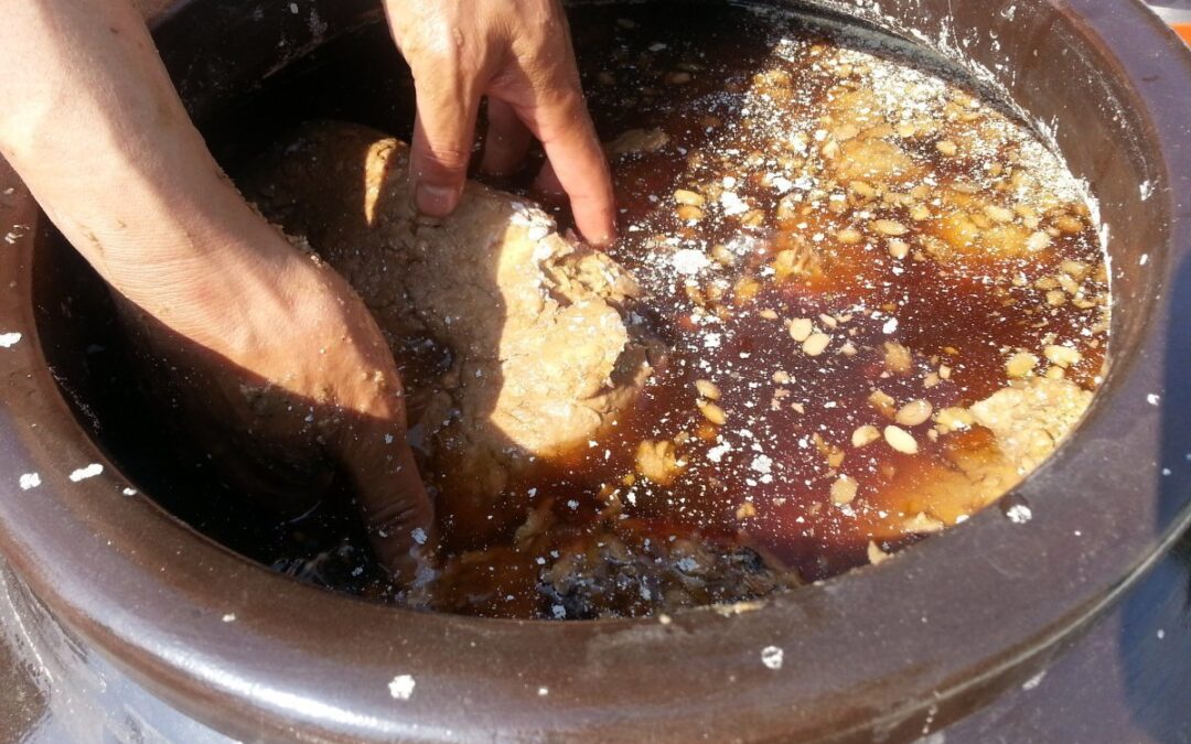 Hands mixing fermented soybean paste in crock.