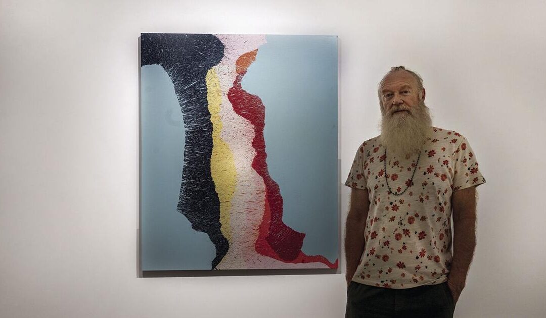 Artist poses beside abstract painting.