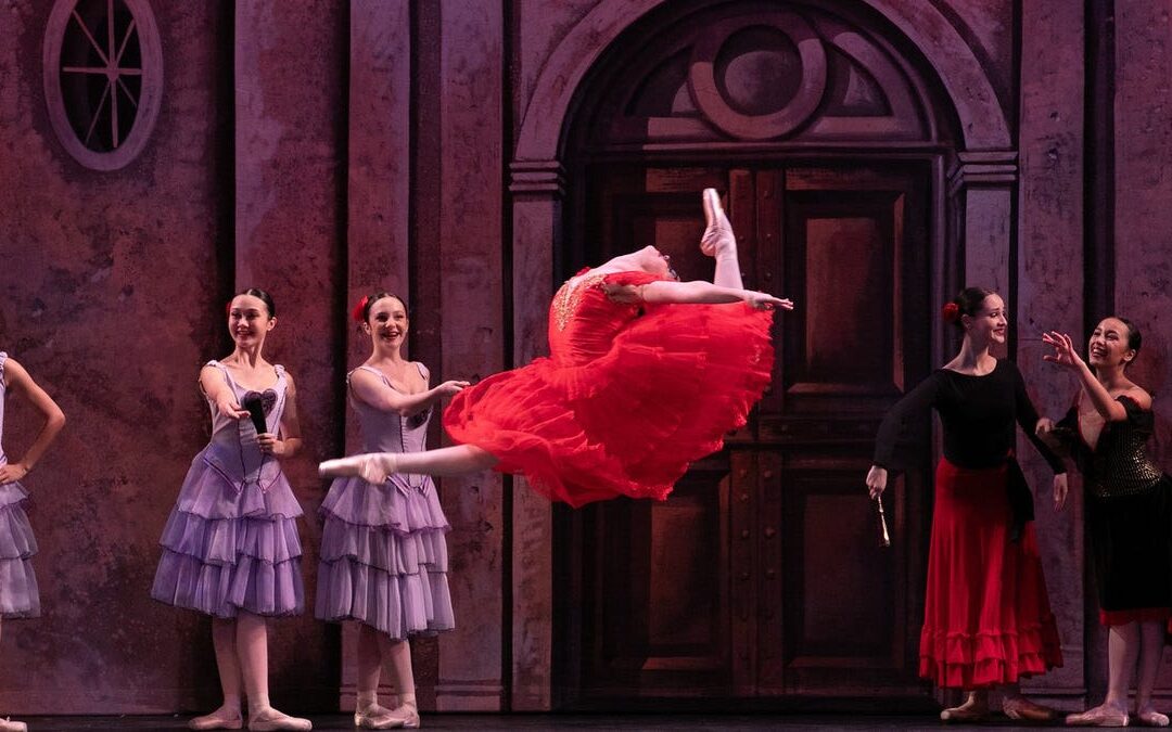 Ballet dancer in red dress leaping on stage.