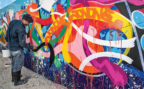 Artist painting colorful graffiti on outdoor wall.