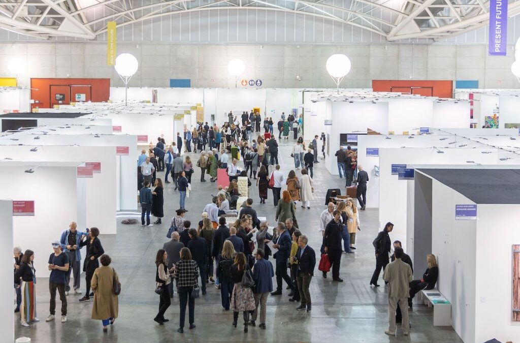Crowded exhibition hall with people attending art fair.
