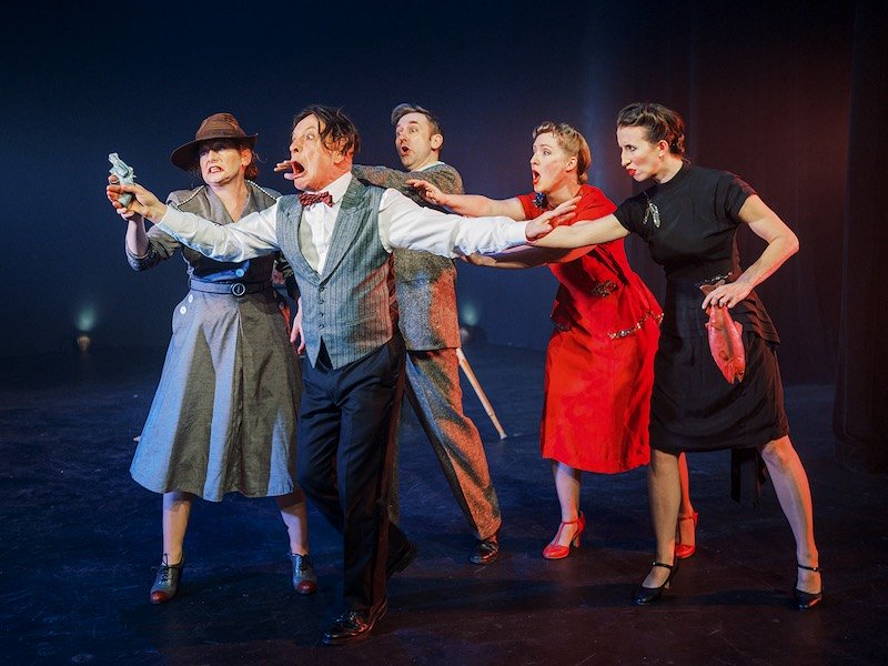 Actors performing dramatic stage scene with toy gun.