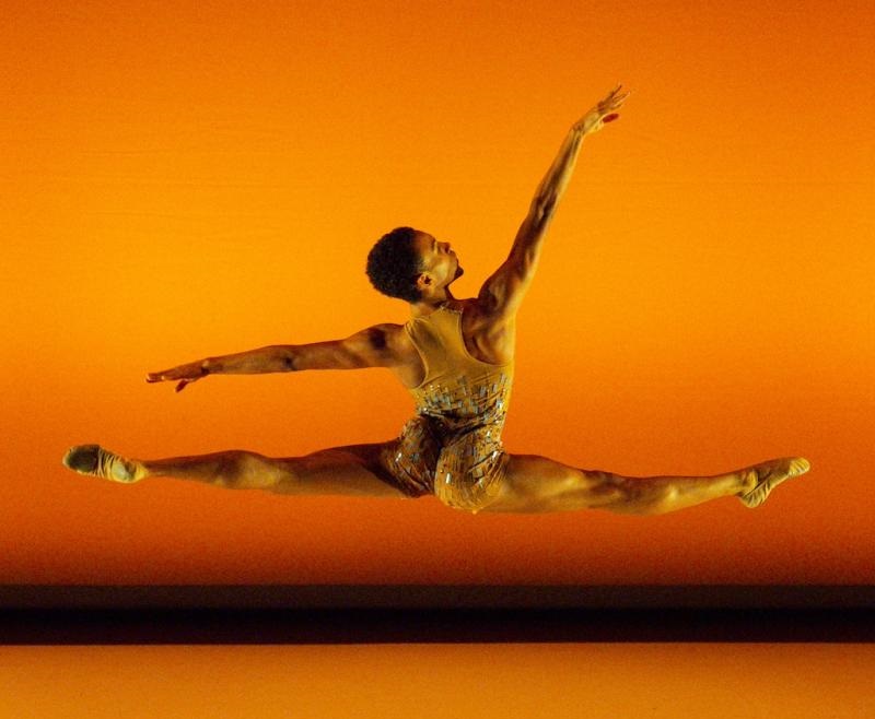 Dancer performs leap against vibrant orange background.
