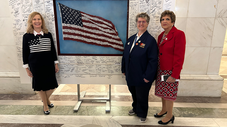 Three women stand beside a large American flag display.