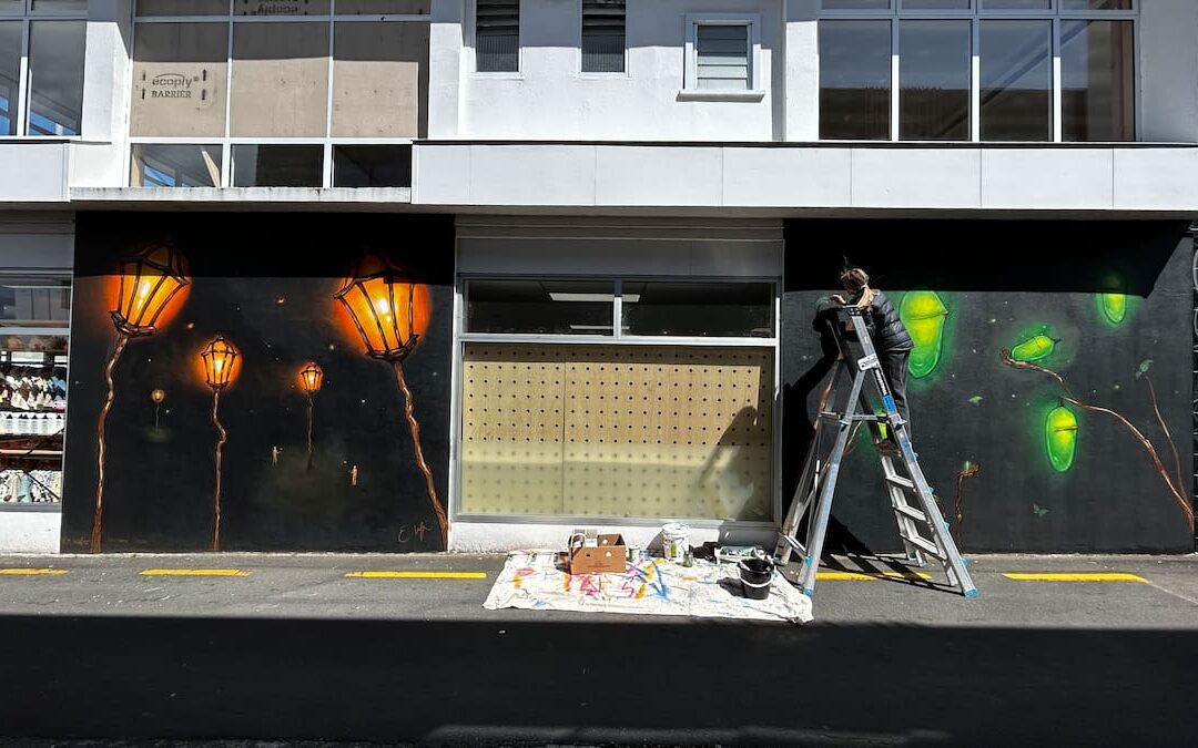 Artist painting street art mural on building wall.