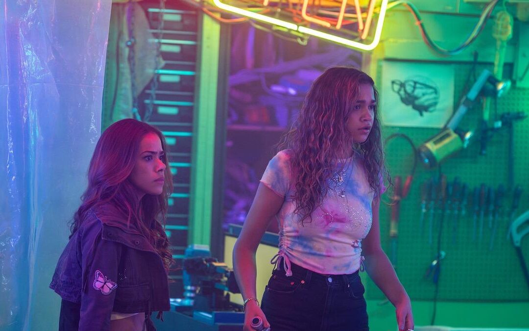 Two women stand in colorful, neon-lit workshop.