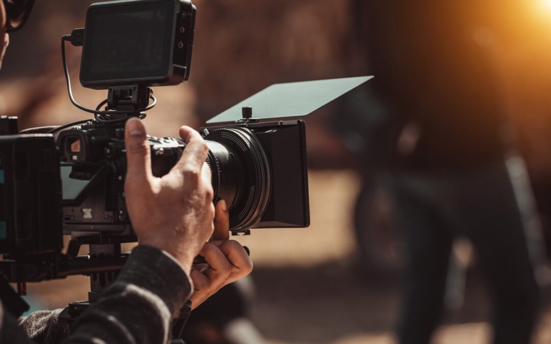 Hands operating a professional video camera outdoors.