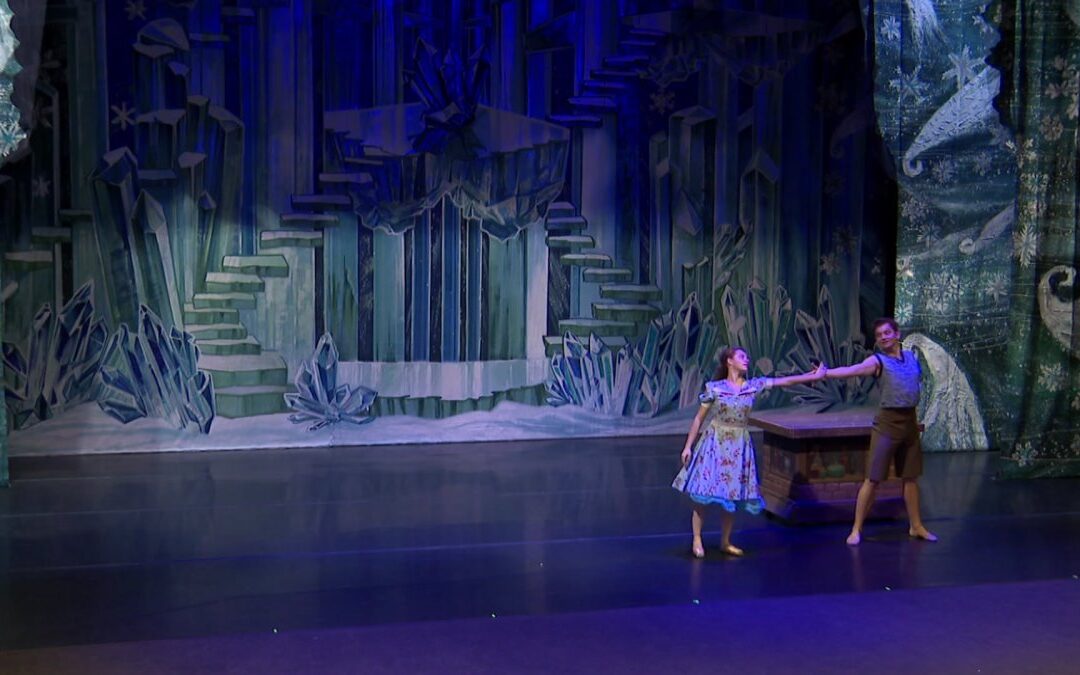 Dancers perform on stage with icy backdrop.
