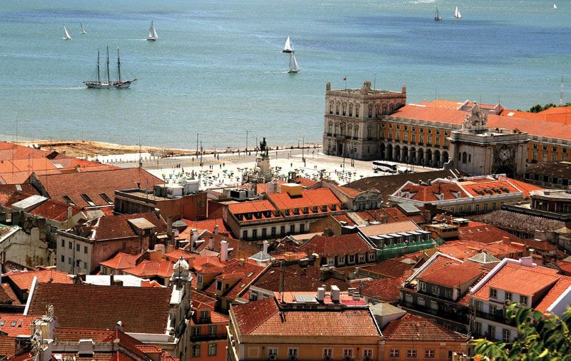 Lisbon waterfront with sailboats and historic buildings.