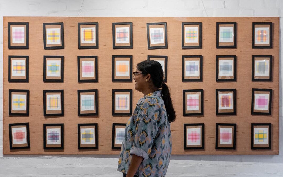 Woman observing framed abstract art pieces on wall.