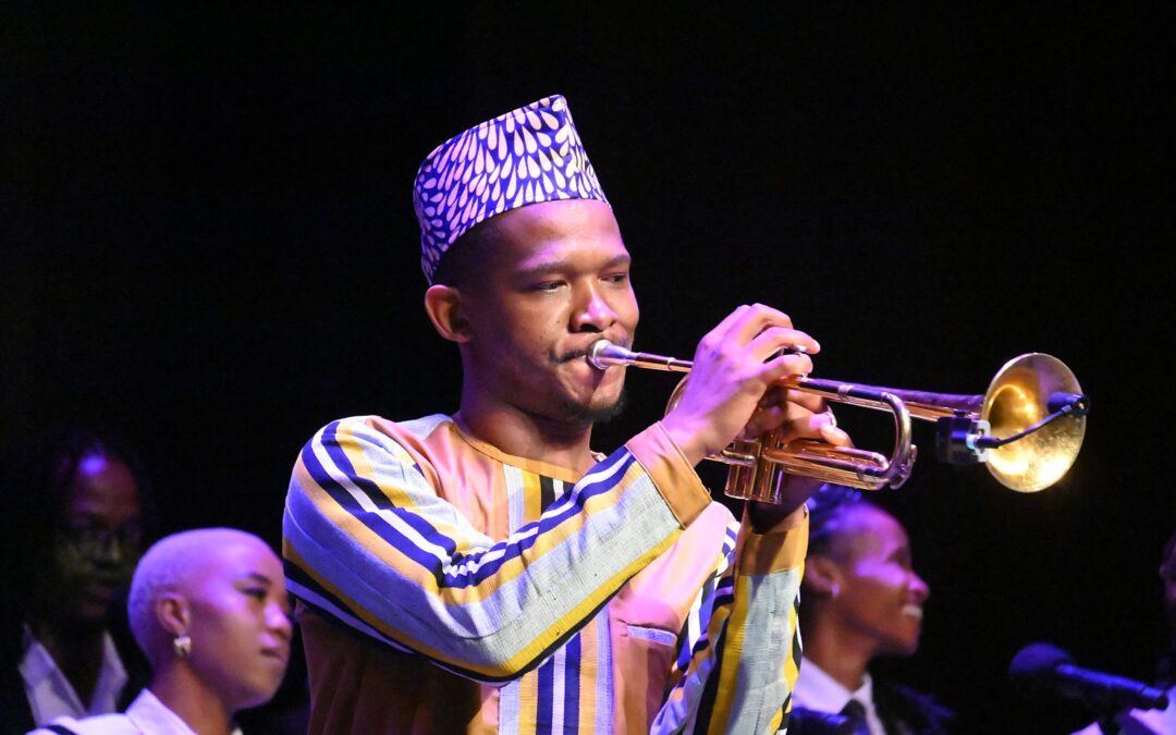 Musician plays trumpet on stage in colorful attire.