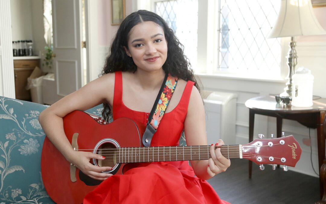 Woman in red dress playing red acoustic guitar.