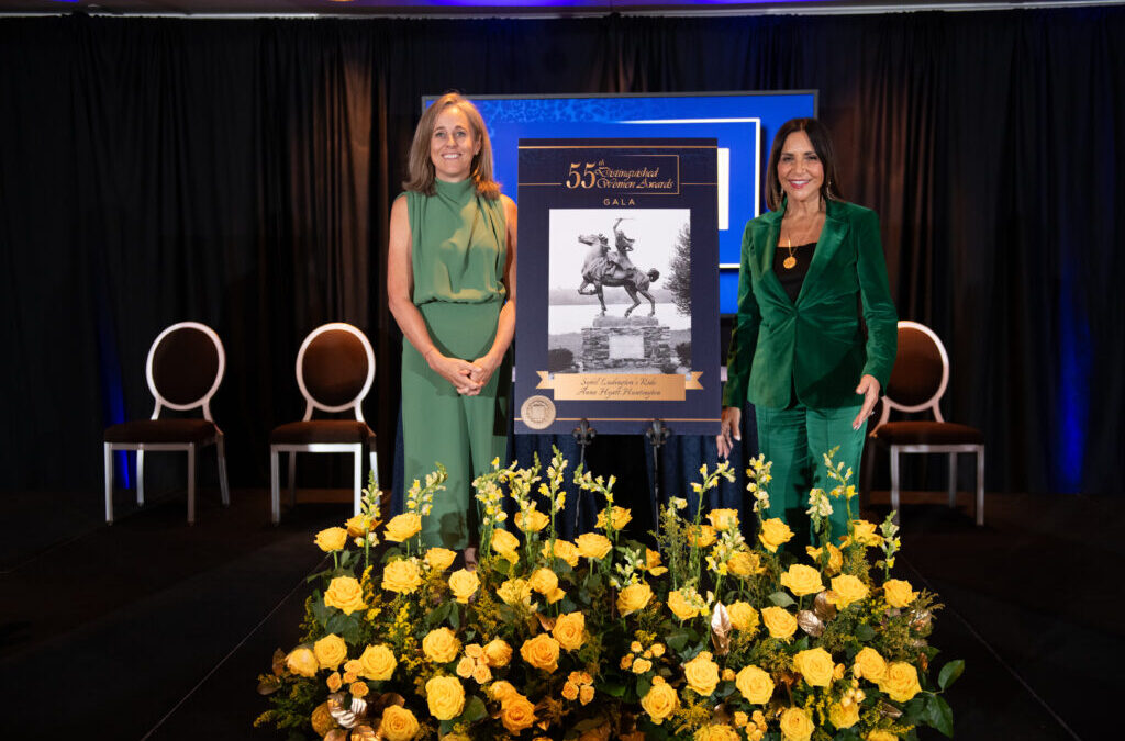 Two women stand by an award poster and flowers.