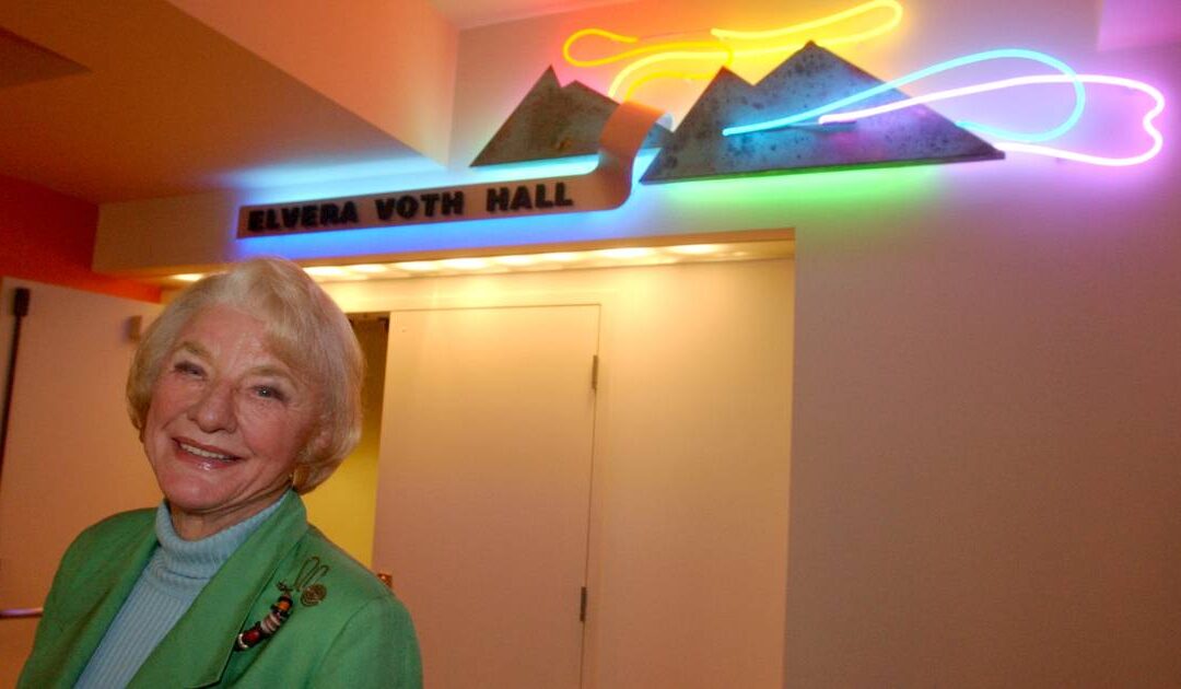 Smiling woman in front of neon Elvera Voth Hall sign.