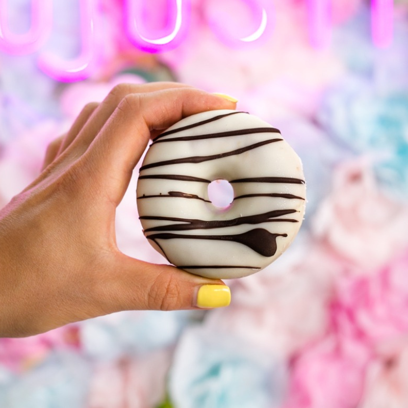 antojos fit Hand holding chocolate-drizzled donut with pastel background.