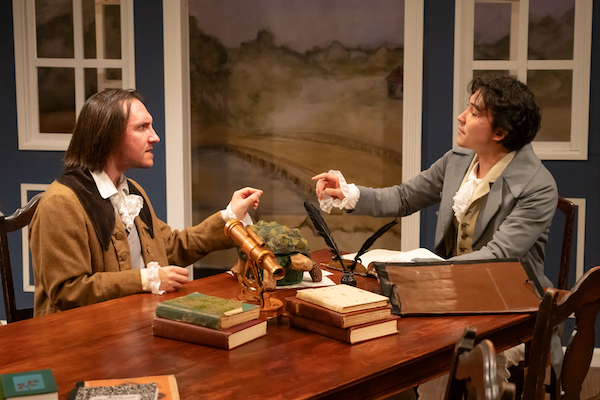 Two actors performing historical scene at theater table.