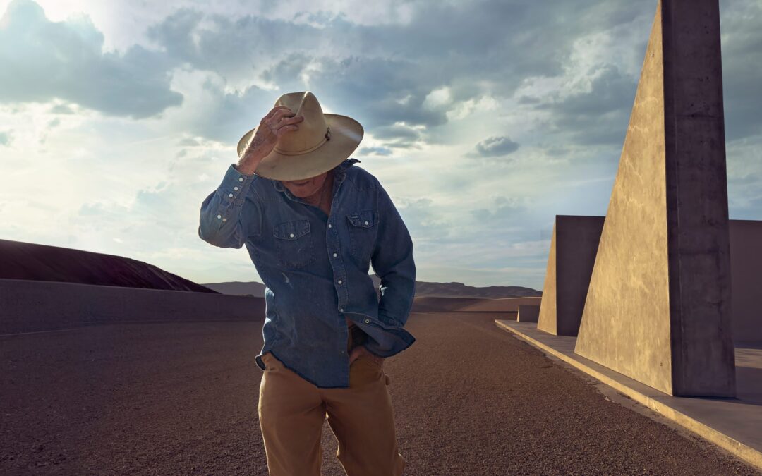 Man in hat in desert landscape with structures.