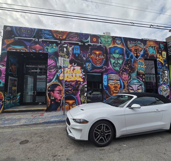 Colorful graffiti mural with white car in front.