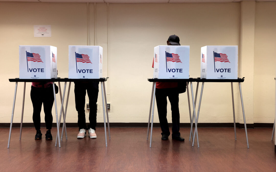 People voting in booths with American flags.