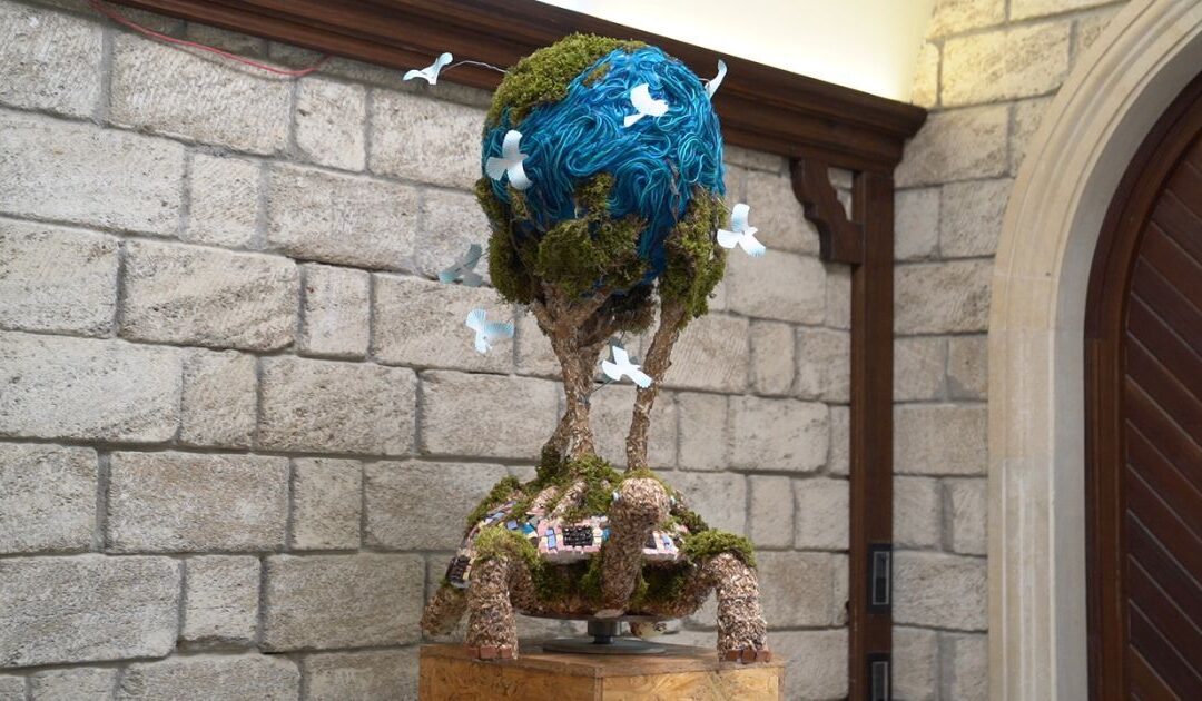 Turtle sculpture with globe and birds in stone room.
