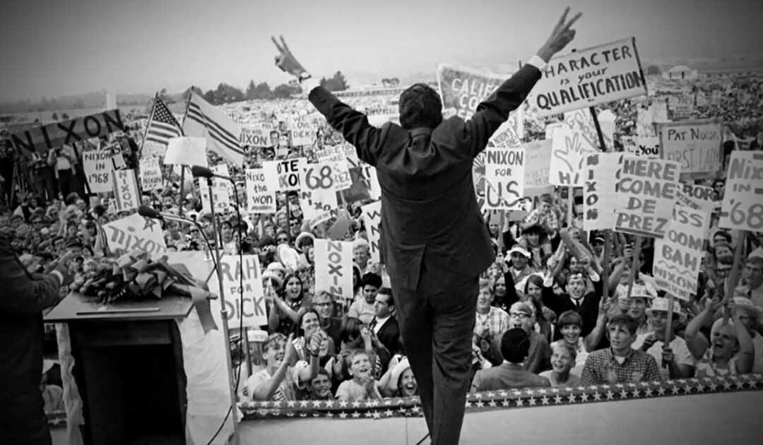 Political rally with crowd holding Nixon signs.