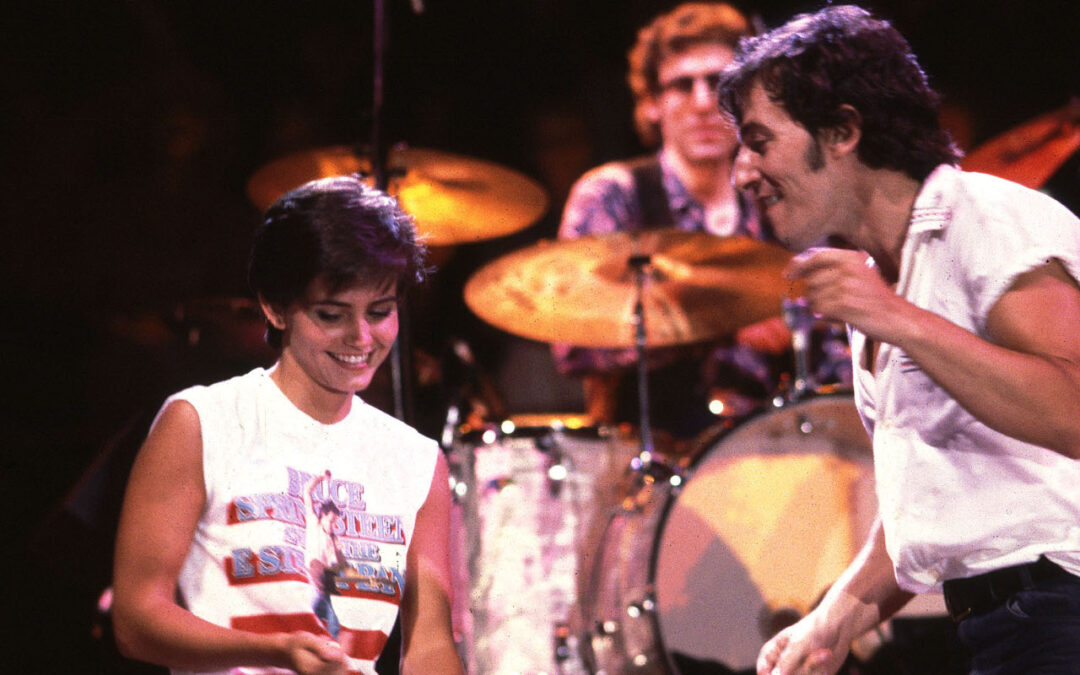 Performers on stage with drum set background.