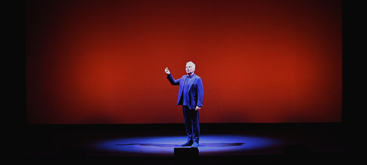 xr:d:DAFj0aYhRlc:3,j:47818090031,t:23052409 Person standing on stage with red background.